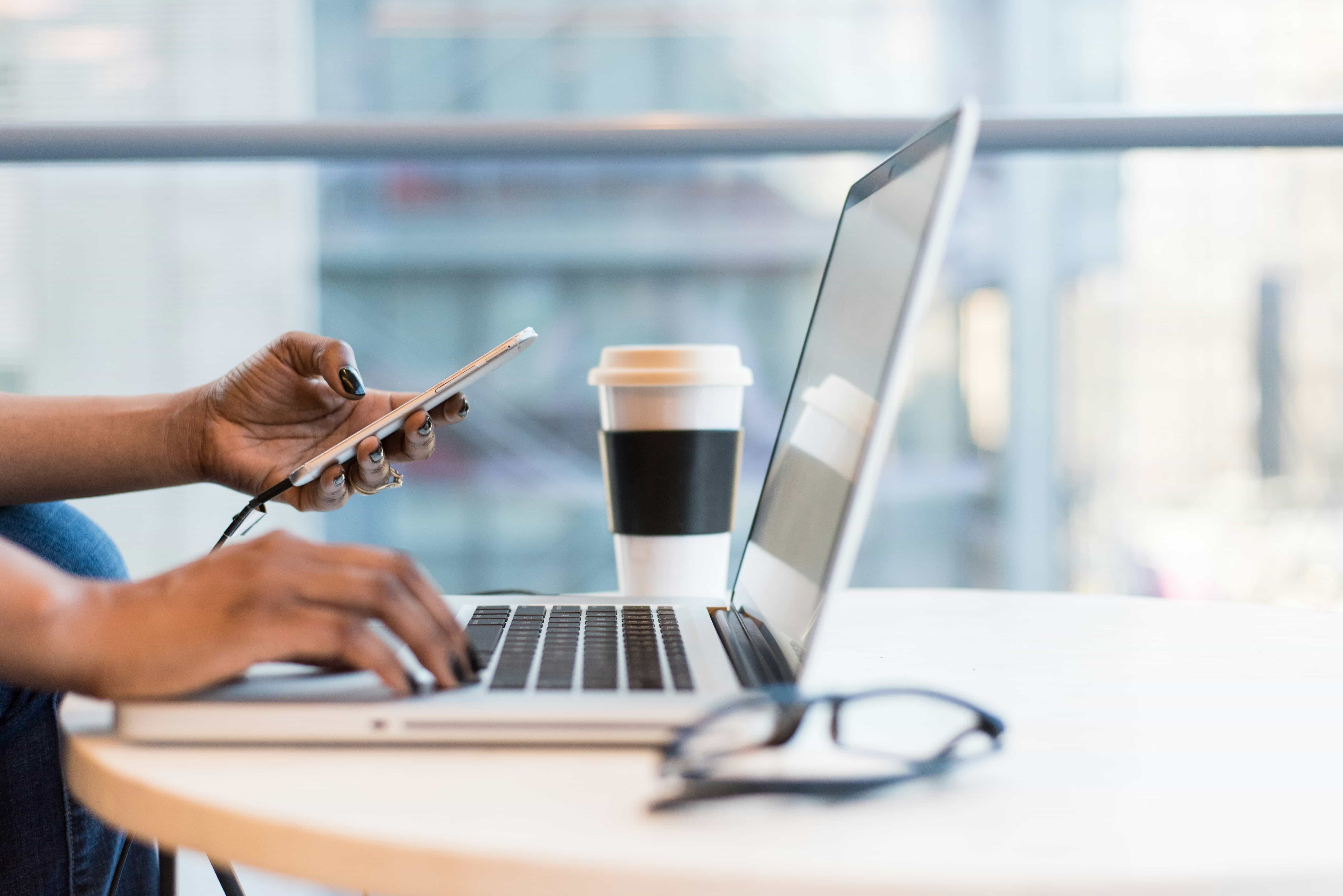 Person working on a laptop with a phone and coffee
